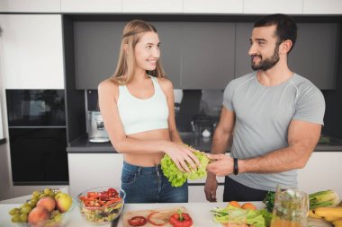 Bir çift bir salata kahvaltı için hazırlanıyor. Bir kız için bir salata sebze keser ve bir adam ona yardımcı olur.