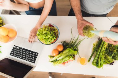 Genç çift mutfakta. Bir adam bir yeşil sebze kokteyl hazırlama.
