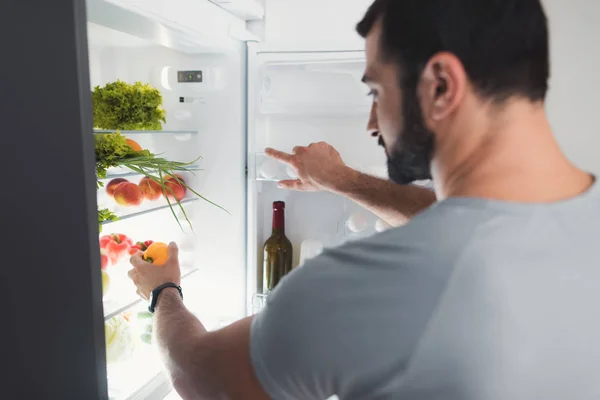 Un deportista se para en la cocina y toma verduras frescas del refrigerador . —  Fotos de Stock