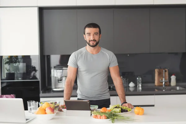Атлетик позирует на кухне. Перед ним на столе различные овощи и фрукты . — стоковое фото