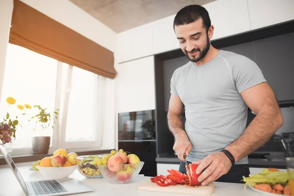 En ung atletisk man förbereder en läcker sallad grönsaker. Han skär grönsaker. — Stockfoto