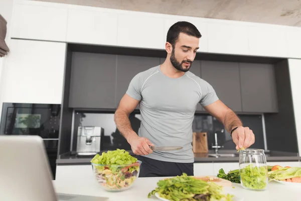 Een sportieve man bereidt een salade in de keuken. Hij snijdt de bladeren van de sla en zet ze in een pot. — Stockfoto