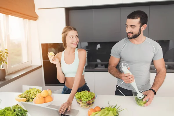 Молодая спортивная пара готовится утром на кухне. Мужчина делает зеленый овощной коктейль . — стоковое фото