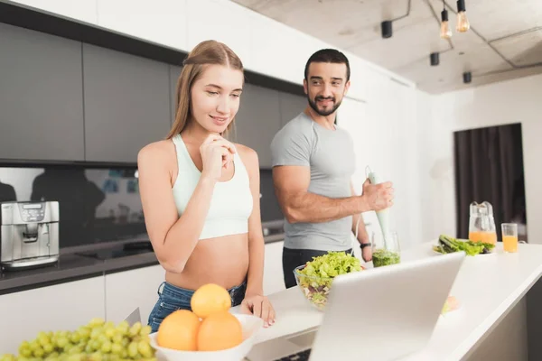 Young sports couple is preparing in the morning in the kitchen. A man is making a green vegetable cocktail. — Stock Photo, Image