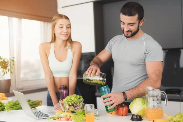 A man and a woman in the kitchen in the morning. The man cooked a green vegetable cocktail and poured it to the woman. — Stock Photo, Image