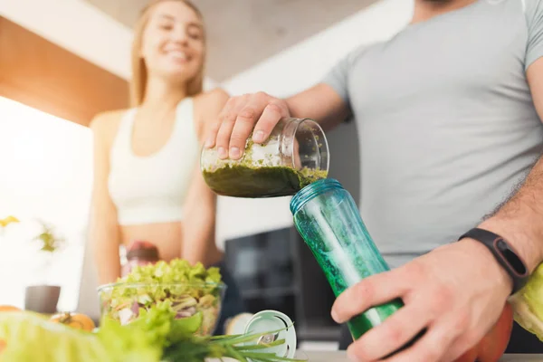 Een man en een vrouw in de keuken in de ochtend. De man gekookt een groene groente cocktail en goot het aan de vrouw. — Stockfoto