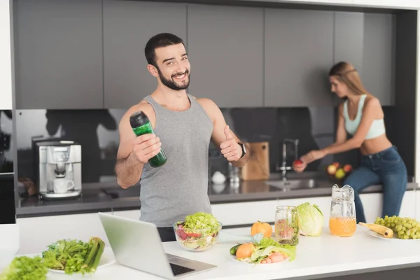 Een man en een vrouw in de keuken in de ochtend. Een man zal spelen met een groene groente cocktail in zijn handen. — Stockfoto
