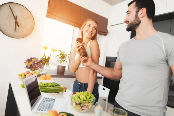 Un uomo e una donna in cucina la mattina. Un uomo giocherà con un cocktail di verdure verdi nelle sue mani . — Foto Stock