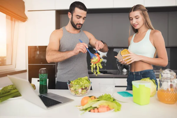 Un homme et une femme dans la cuisine le matin. L'homme est en train de mettre une salade sur les vaisseaux . — Photo