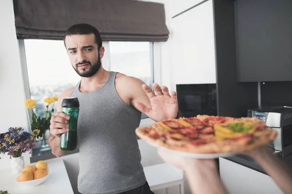 Un hombre y una mujer en la cocina por la mañana. Un hombre bebe un cóctel de verduras y rechaza la pizza propuesta . —  Fotos de Stock
