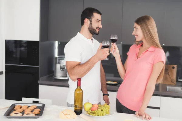 Een man en een vrouw zijn wijn drinken in de keuken. Zij houden glazen wijn in hun handen. — Stockfoto