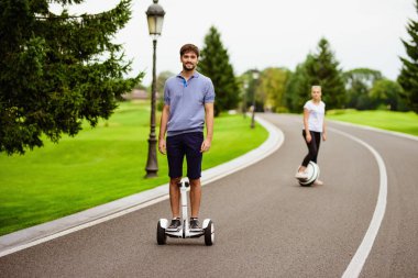 Çift bir gyroboard ve bir tek gözlük parkta biniyor. Onlar mutlular. Adam ileri sürme, arkasında bir kadındır.