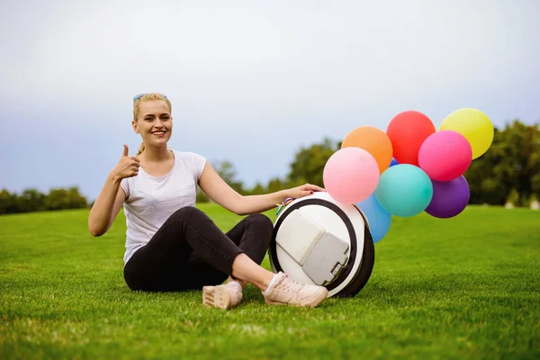 Een vrouw zit op het gras. In de buurt van de monoclean, waarop de opblaasbare ballen zijn aangesloten. — Stockfoto