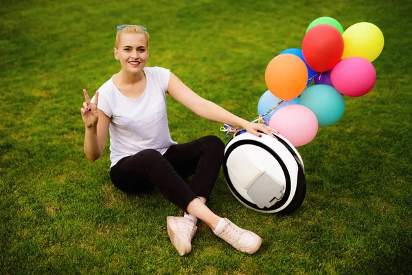 A woman is sitting on the grass. Near the monoclean, to which the inflatable balls are attached. — Stock Photo, Image