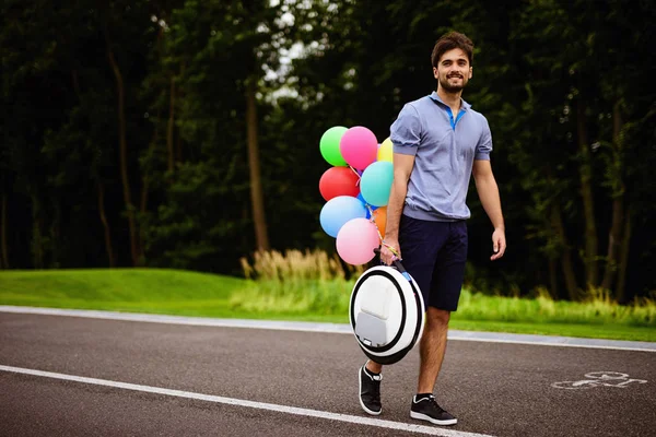 En man går längs sökvägen park med en monoclean i händerna. Att det är fäst flerfärgad uppblåsbara bollar — Stockfoto