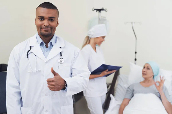 Läkare poserar mot bakgrund av patienten. Han visar en tummen upp. — Stockfoto