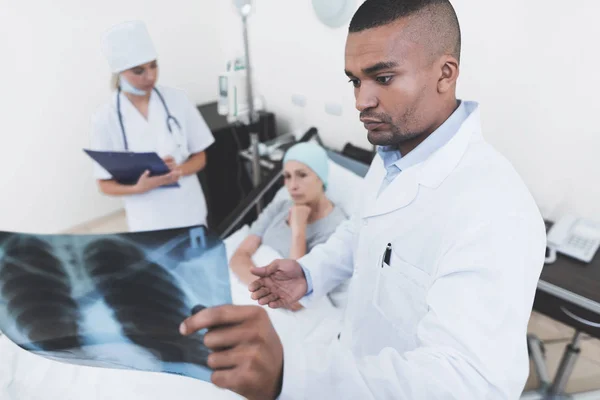 En sjuksköterska är ställning mot patientens bakgrund. Hon håller en papper-tablett i händerna. — Stockfoto