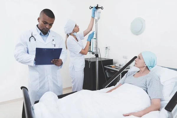 Die Krankenschwester stellt der Frau einen Tropfer. In der Nähe ist ein Arzt, der die Aussage einer krebskranken Frau aufzeichnet. — Stockfoto