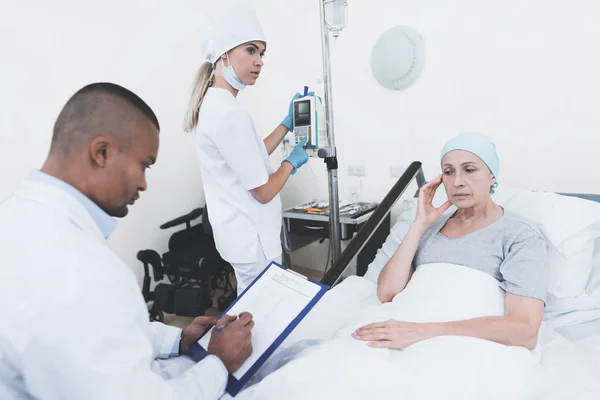 Sköterskan ställer kvinnan en dropper. I närheten finns en läkare som registrerar vittnesmål från en kvinna som har cancer. — Stockfoto