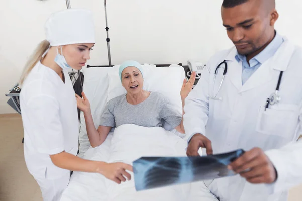 Eine Krankenschwester und ein Arzt stehen neben einer krebskranken Patientin. die Ärztin hält ihr Röntgenbild in der Hand. — Stockfoto