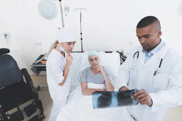 Μια νοσοκόμα και ένας γιατρός στέκεται δίπλα σε έναν ασθενή με καρκίνο. Ο γιατρός κρατάει την ακτινογραφία. — Φωτογραφία Αρχείου