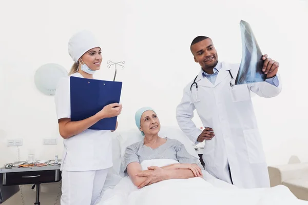 En sjuksköterska och en läkare står bredvid en patient med cancer. Läkaren håller hennes röntgen. — Stockfoto