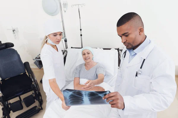 A nurse and a doctor are standing next to a patient with cancer. The doctor is holding her X-ray. — Stock Photo, Image