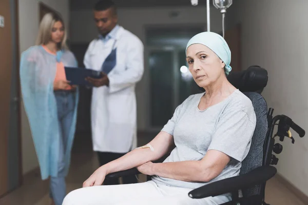 En kvinna med cancer, med en dömd look, sitter i rullstol. Bakom hennes dotter står och pratar med läkaren. — Stockfoto