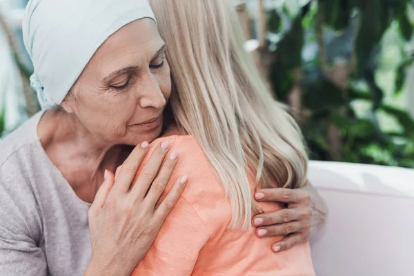 Una mujer con cáncer está sentada en un sofá blanco junto a su hija. Una chica está abrazando a una mujer —  Fotos de Stock