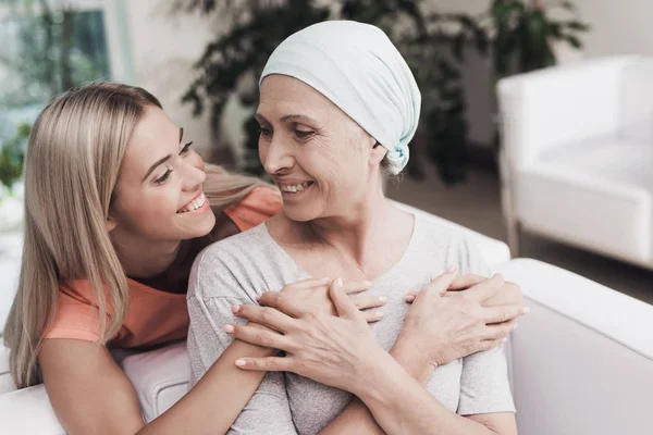 Una mujer con cáncer está sentada en un sofá blanco junto a su hija. Una chica está abrazando a una mujer —  Fotos de Stock