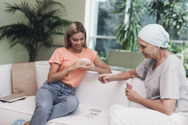 Una mujer con cáncer está sentada en un sofá blanco en una clínica moderna. Junto a ella se sienta su hija . —  Fotos de Stock