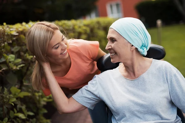 Een vrouw met kanker zit in een rolstoel. Ze loopt op straat met haar dochter en ze plezier. — Stockfoto