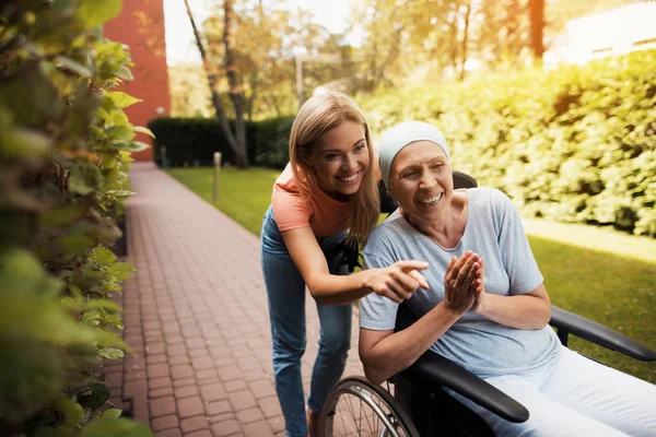 Een vrouw met kanker zit in een rolstoel. Ze loopt op straat met haar dochter en ze plezier. — Stockfoto