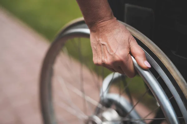 癌を持つ女性は、車椅子に座っています。彼女は彼女が置かれる車椅子の車輪の後ろに彼女の手を保持しています。. — ストック写真