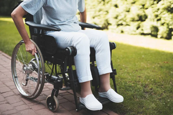 Uma mulher com cancro está sentada numa cadeira de rodas. Ela segura as mãos atrás das rodas da cadeira de rodas em que se senta . — Fotografia de Stock