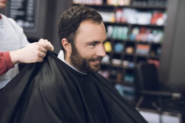 Bir adam bir erkek berber, saçını kesmek için geldiği bir berber sandalyede oturuyor.