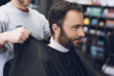 Bir adam bir erkek berber, saçını kesmek için geldiği bir berber sandalyede oturuyor.