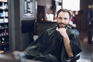 Bir adam bir erkek berber, saçını kesmek için geldiği bir berber sandalyede oturuyor.