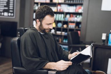 Bir adam bir erkek berber, saçını kesmek için geldiği bir berber sandalyede oturuyor.