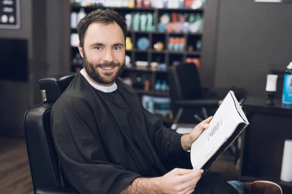 Un hombre se sienta en la silla de un barbero en la peluquería de un hombre, donde vino a cortarse el pelo . — Foto de Stock