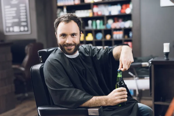 En man dricker alkohol i den frisörsalong fåtölj av en modern barbershop. — Stockfoto