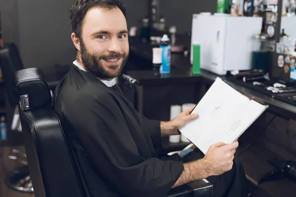 Un hombre se sienta en la silla de un barbero en la peluquería de un hombre, donde vino a cortarse el pelo . — Foto de Stock