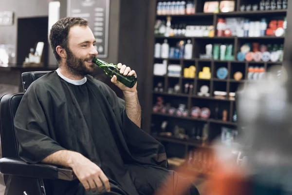 Un homme boit de l'alcool dans le fauteuil d'un salon de coiffure moderne . — Photo