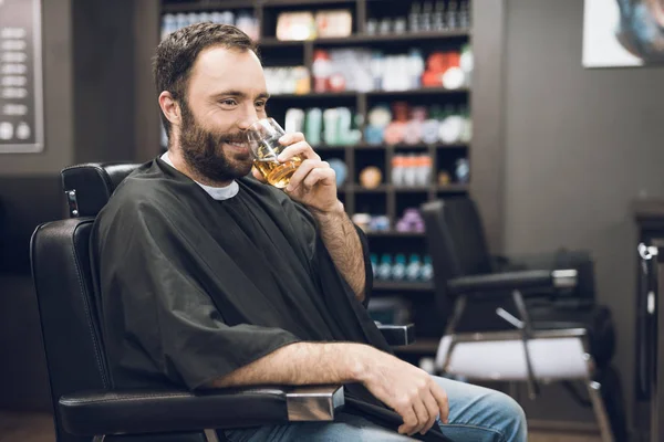 Człowiek pije alkohol w fotel fryzjerski z nowoczesny salon fryzjerski. — Zdjęcie stockowe