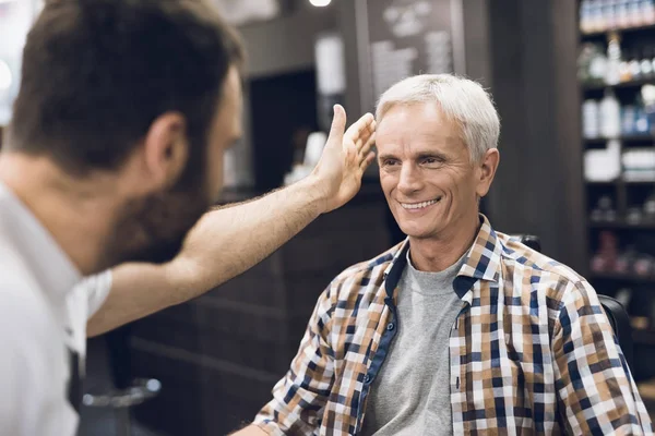 Gubben sitter i barberarens stol i en mans barbershop, där han kom att klippa sitt hår. — Stockfoto