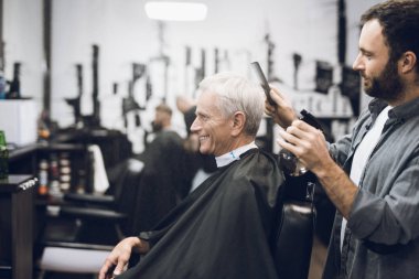 The hairdresser does a hairstyle to an old man with gray hair in a barbershop. clipart