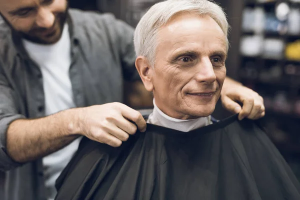 De oude man zit in de Barbers stoel in een man's barbershop, waar hij kwam om zijn haar te snijden. — Stockfoto