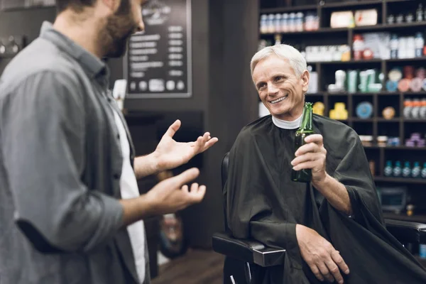 Den gamla mannen dricker alkohol i barberarens stol i barbershop. — Stockfoto