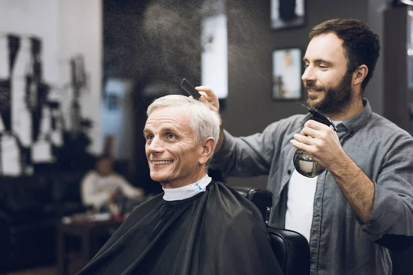 De kapper doet een kapsel met een oude man met grijs haar in een kapsalon. — Stockfoto