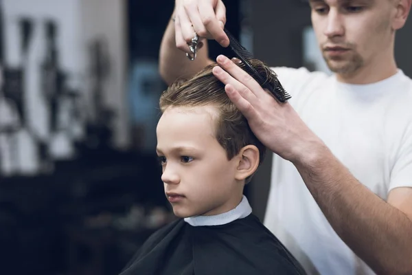 The hairdresser makes a fashionable pretty hairstyle for the boy in a modern barbershop. — Stock Photo, Image